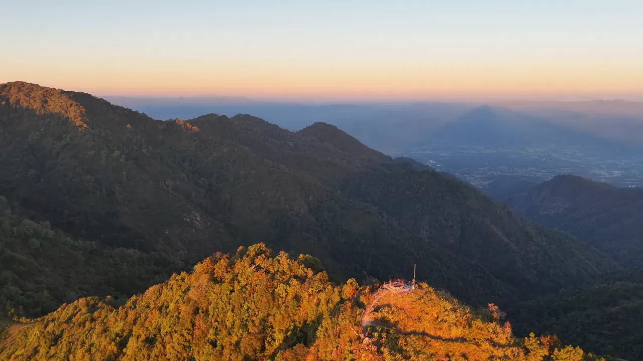 Low sun turning a forested summit orange, with the mountains beyond