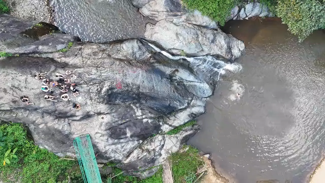 Mor Pang Waterfall from above: people on the rock beside the falls, the pool and the green walkway