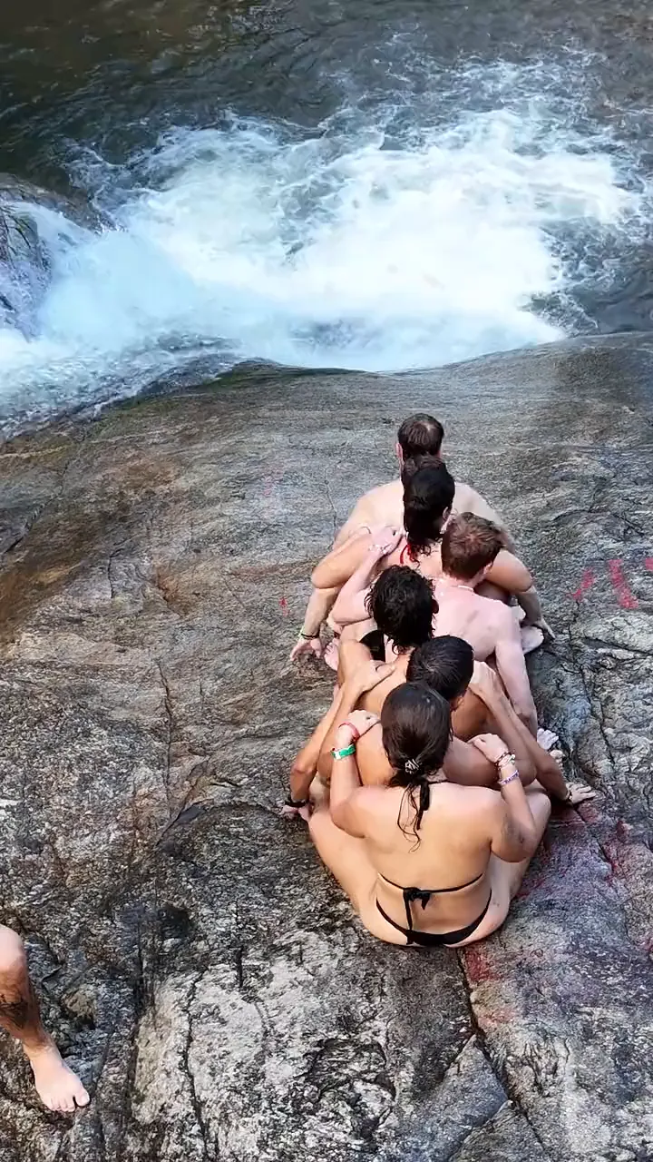A Nolo Hub Pai group sitting in a line on the rock slide at Mor Pang Waterfall, sliding down together into the pool