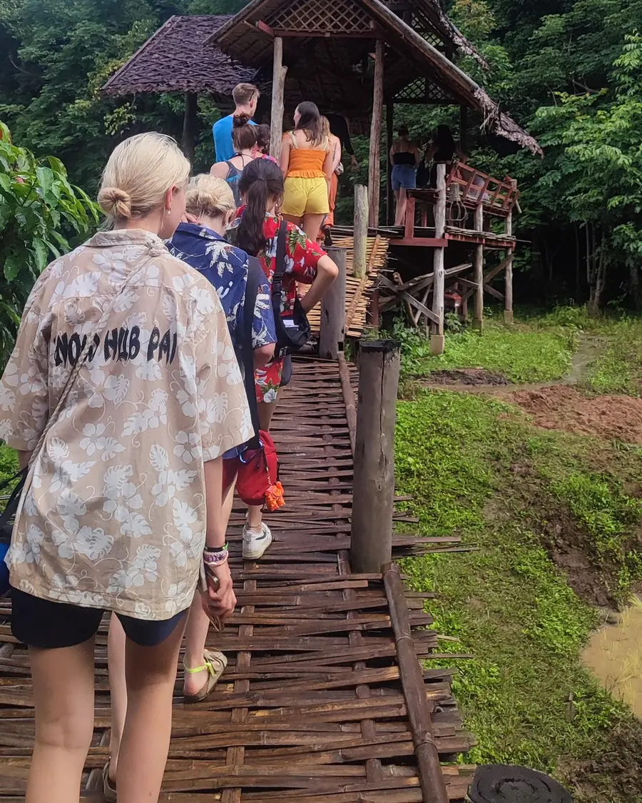 A Nolo Hub group walking the Bamboo Bridge towards a hut, one in a Nolo Hub Pai shirt