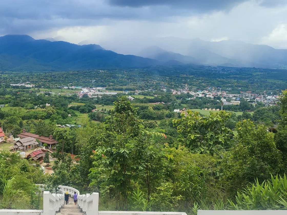 Pai town and the green valley floor seen from the top of the White Buddha’s white stairway in August, with rain falling over the mountains behind