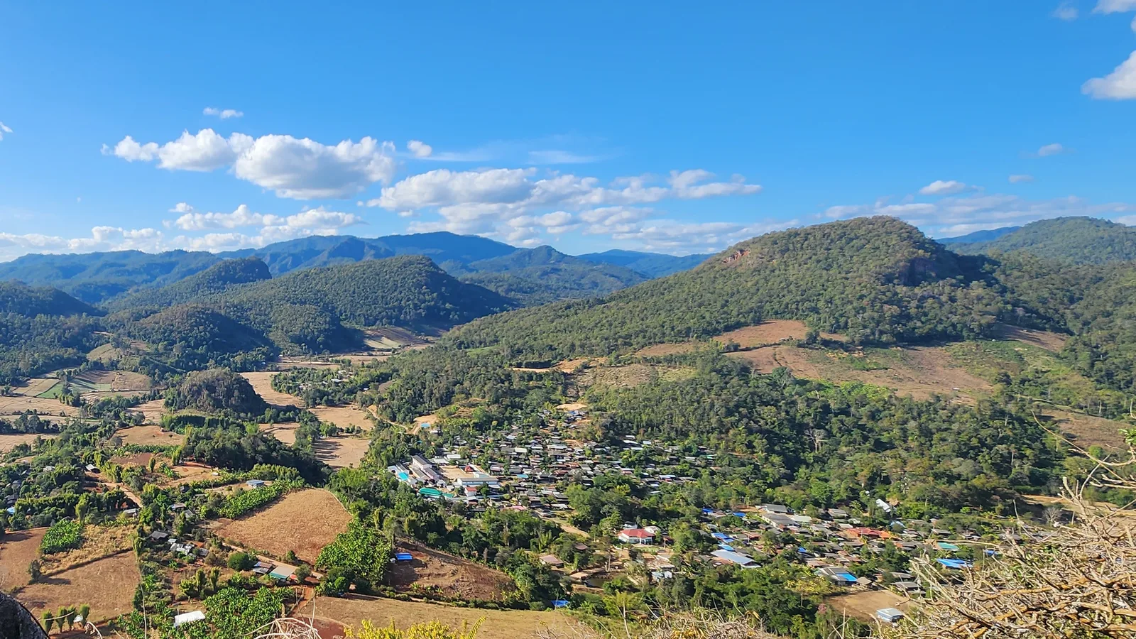 A village among brown fields and green hills north of Wiang Nuea under a clear blue January sky