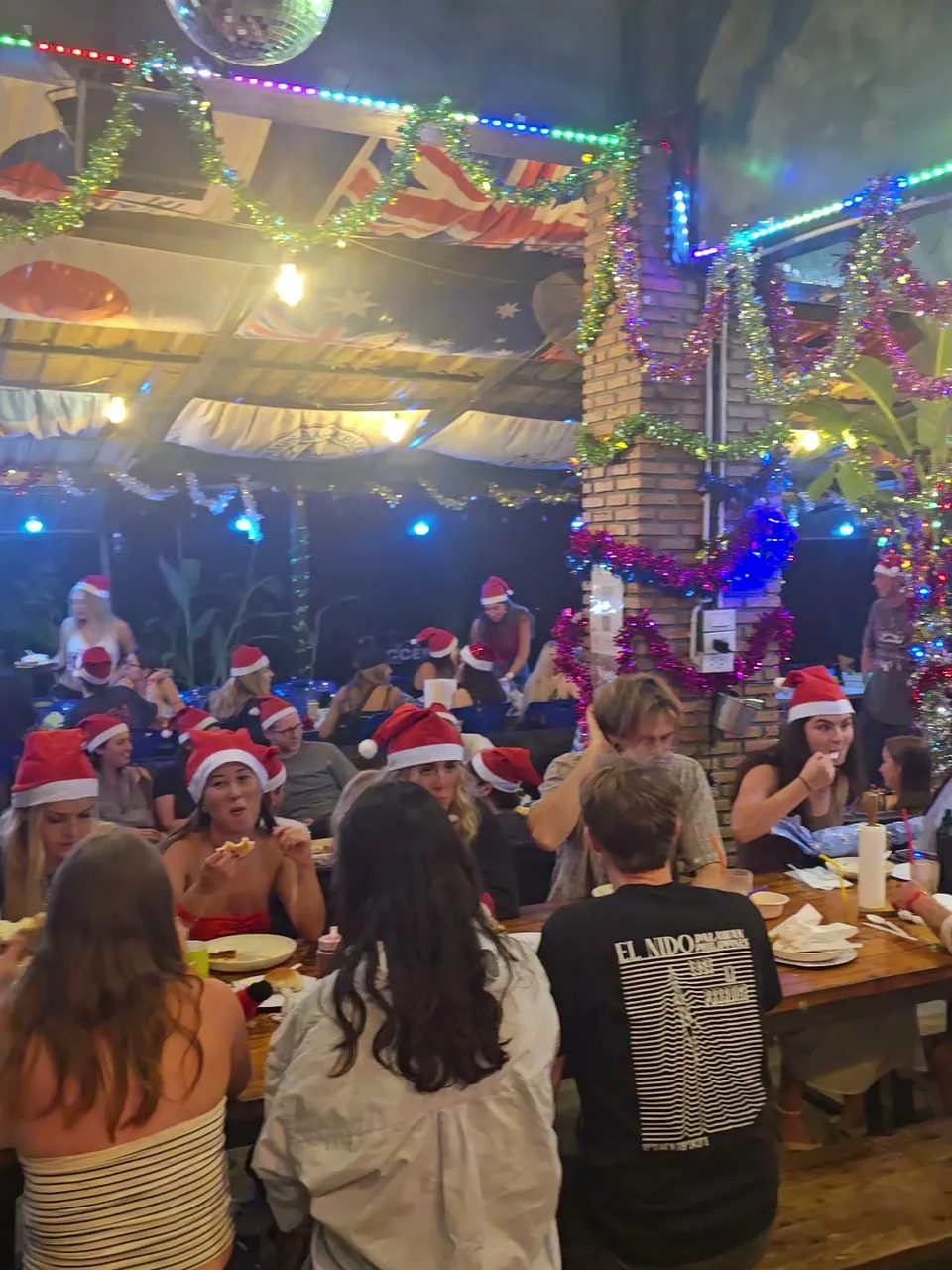 Long tables full of people in Santa hats eating Christmas dinner at Nolo Hub Pai under tinsel, coloured lights and a mirror ball