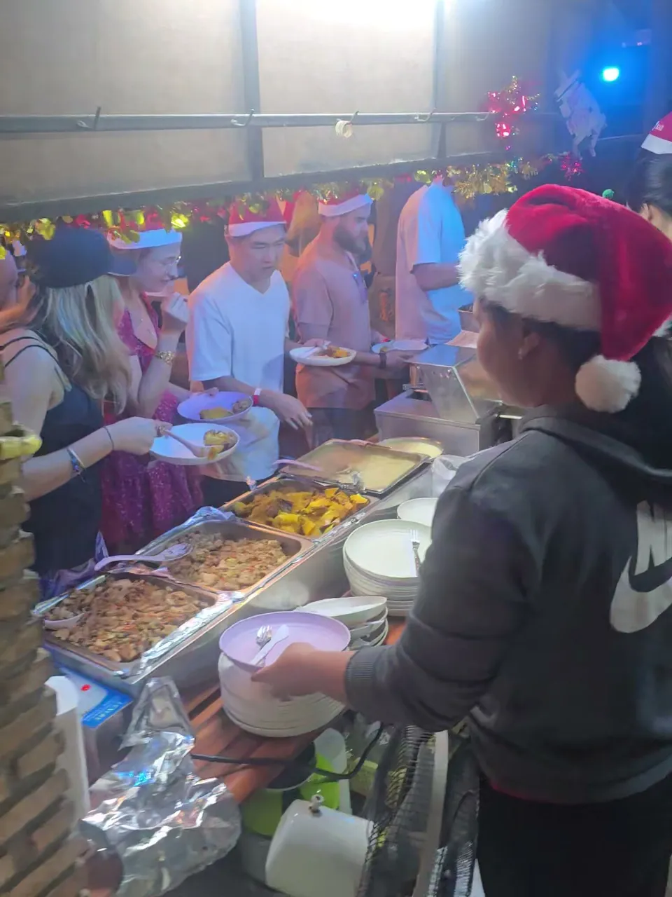 Guests in Santa hats filling their plates along the Christmas dinner buffet at Nolo Hub Pai, a member of the team in a Santa hat in front