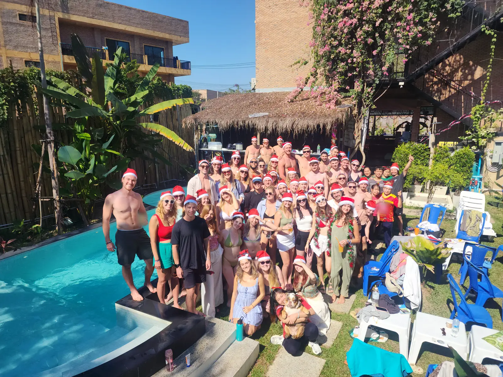 A big crowd of guests in Santa hats around the pool at Nolo Hub Pai on a sunny Christmas Day, a staff member holding a bulldog at the front