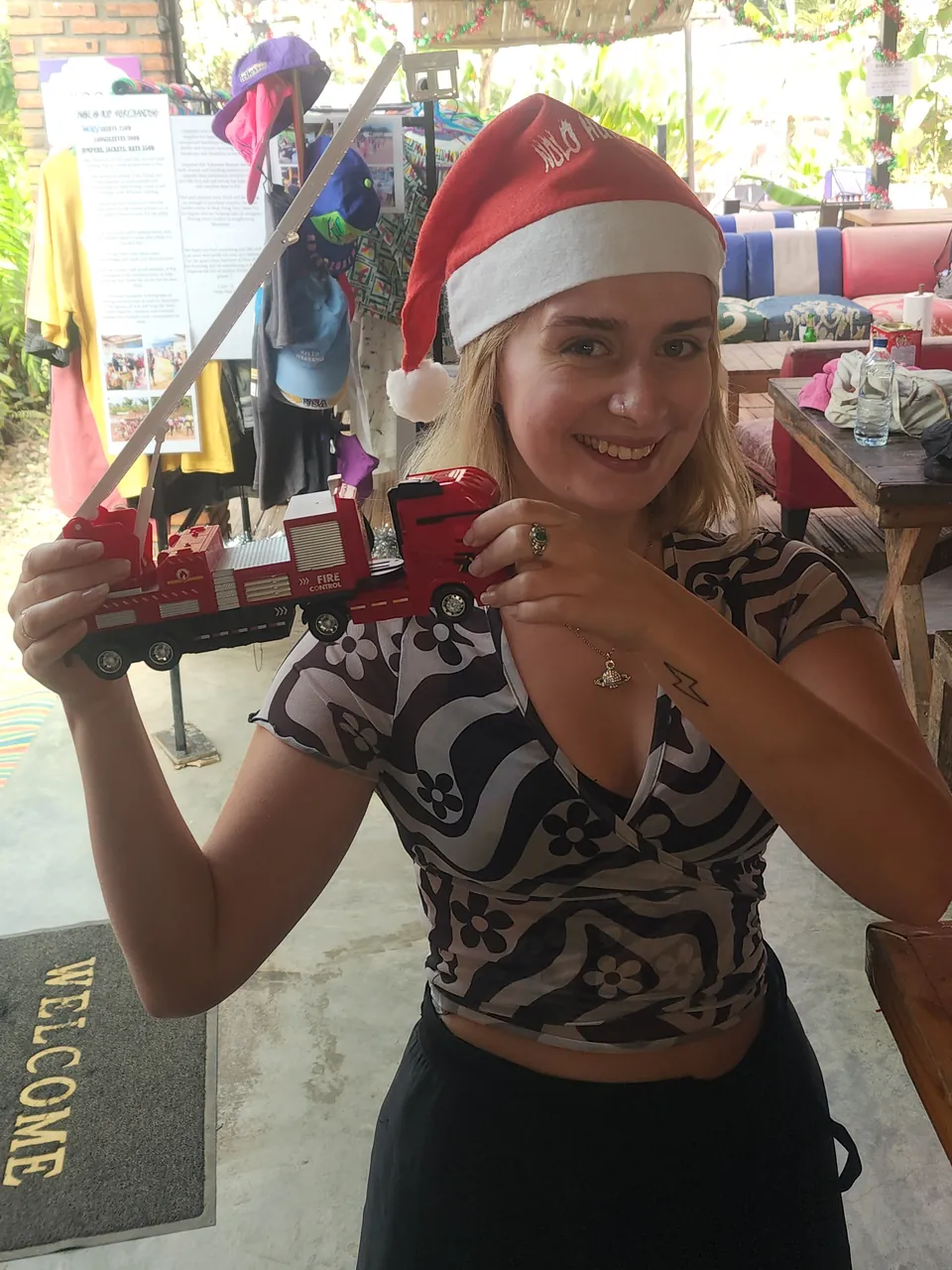 A guest in a Santa hat holding up her Secret Santa present, a toy fire engine, in the common area at Nolo Hub Pai