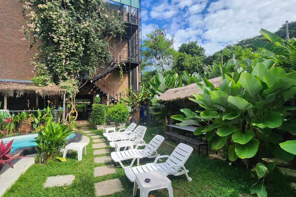 The garden at Nolo Hub: loungers along a stepping-stone path, a thatched shelter and the edge of the pool