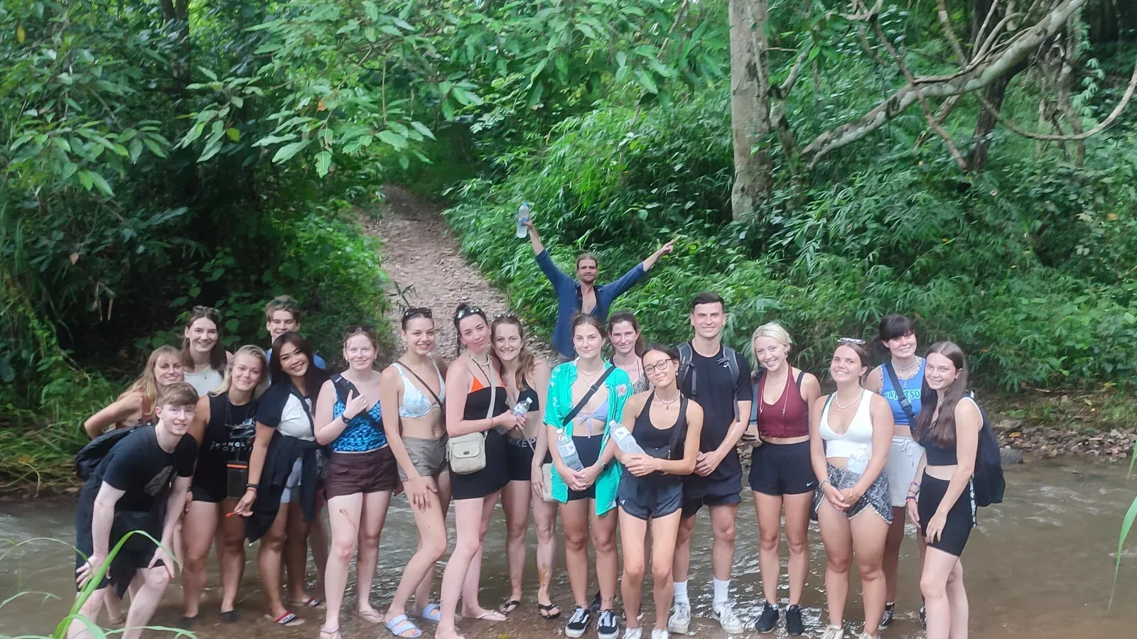 A group standing in the river on the Hua Chang trail, with the path climbing into the forest behind