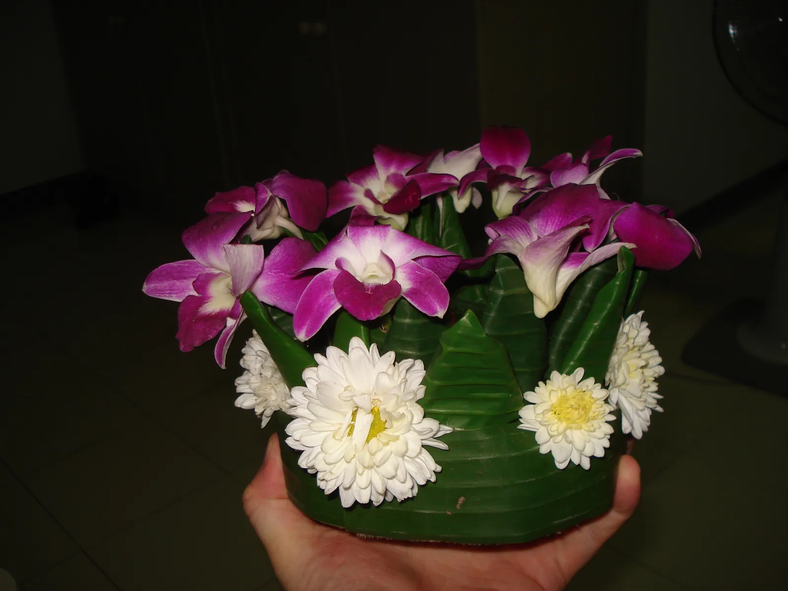 A hand-made krathong of banana trunk and folded banana leaves, topped with orchids and white flowers, held in one hand