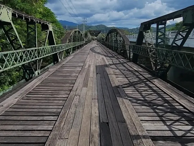 The wooden deck of the Pai Memorial Bridge running between green steel trusses
