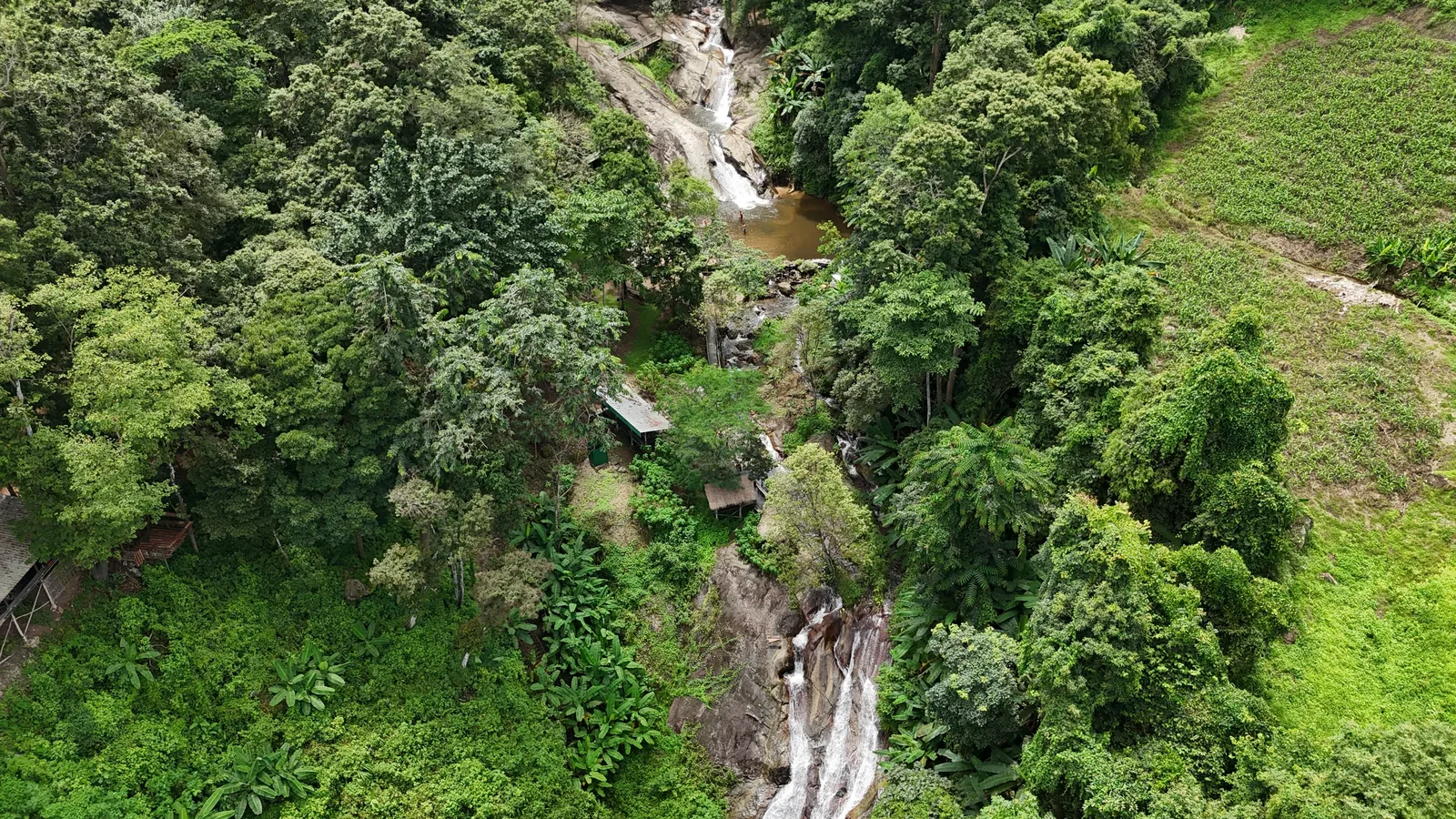 The Mor Pang falls in the forest, with farmland on the hillside beside them