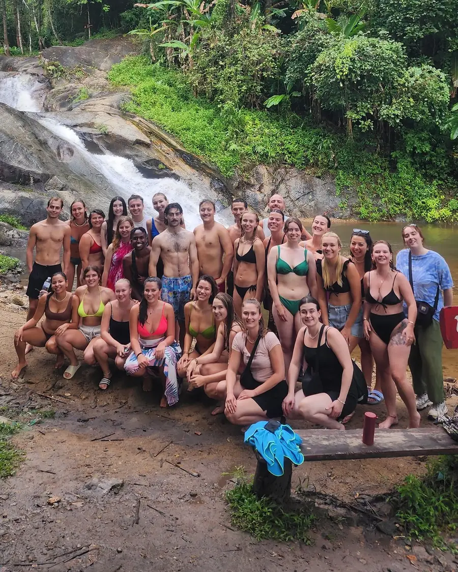 A Nolo Hub group on the rocks below Mor Pang Waterfall, with the falls behind