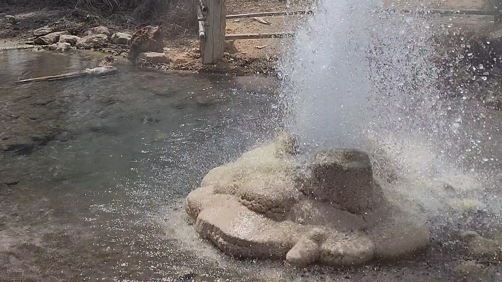 The well at Muang Rae spouting from its mound of mineral crust, with the water spreading across the ground