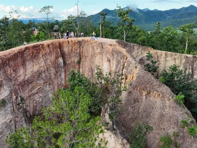 A sheer orange cliff at Pai Canyon, with walkers on the rim and the mountains beyond