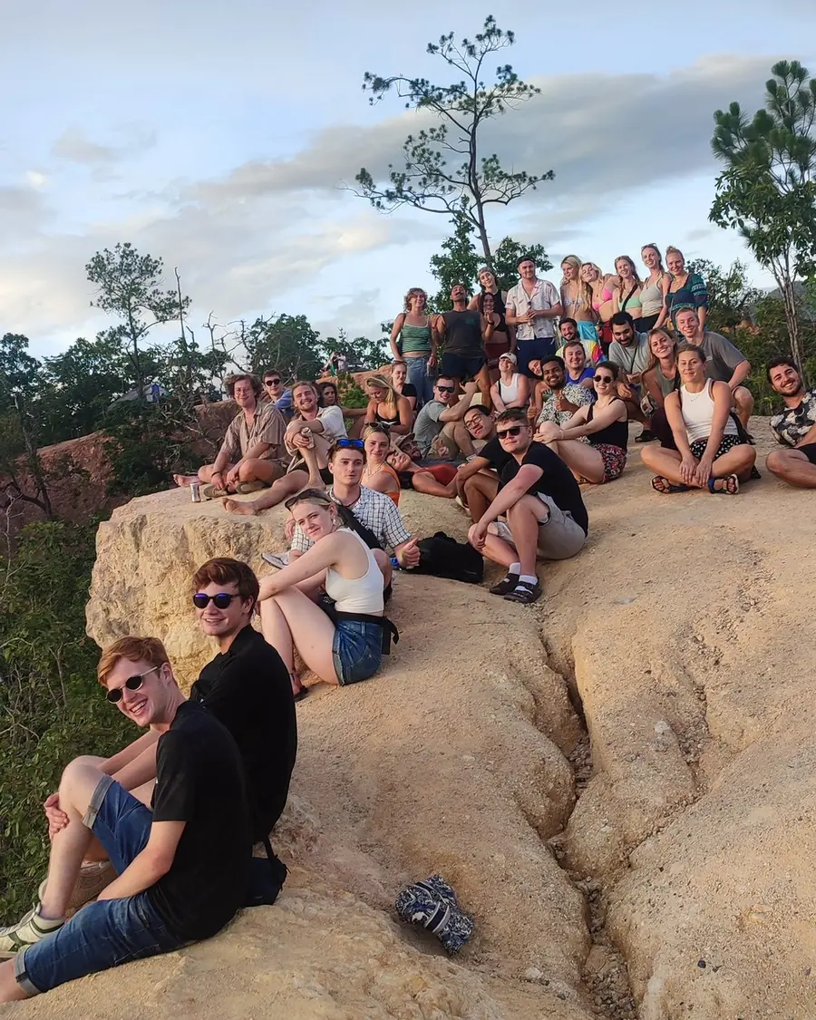 A Nolo Hub group sitting together on a ridge at Pai Canyon, with a pine tree and the evening sky behind