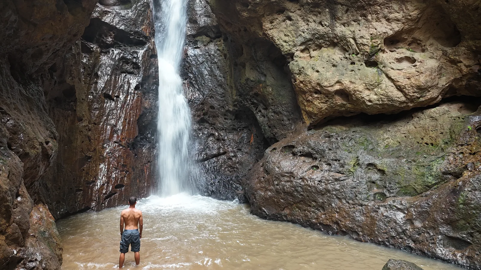 A lone swimmer standing in the pool beneath Pam Bok Waterfall
