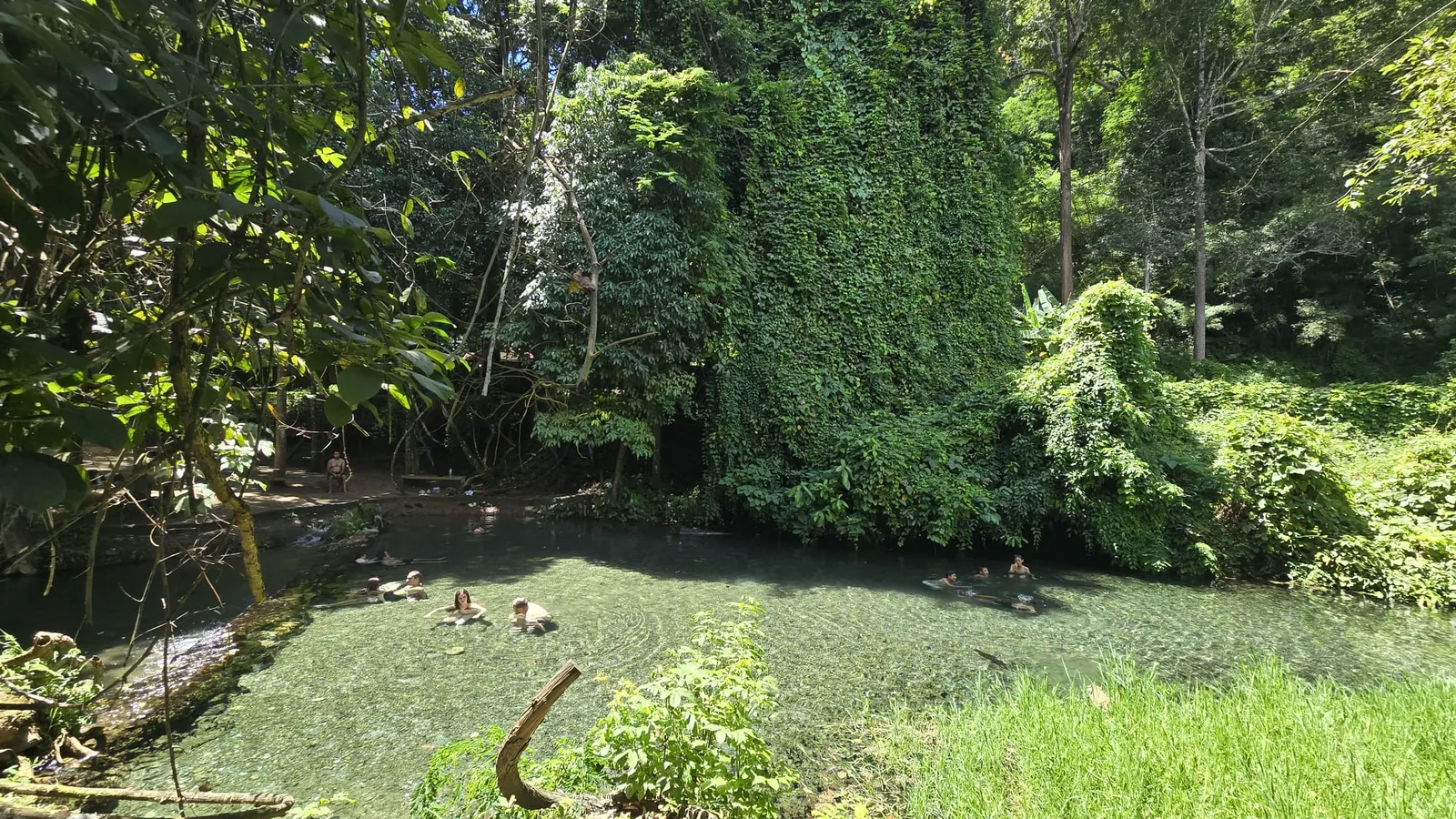 People soaking in Sai Ngam's clear main pool, under a wall of forest