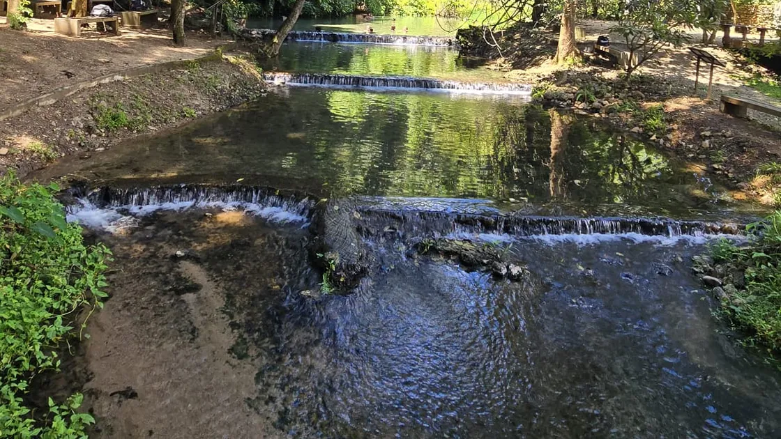 The stream at Sai Ngam stepping down over low stone weirs, with bathers in the pool beyond