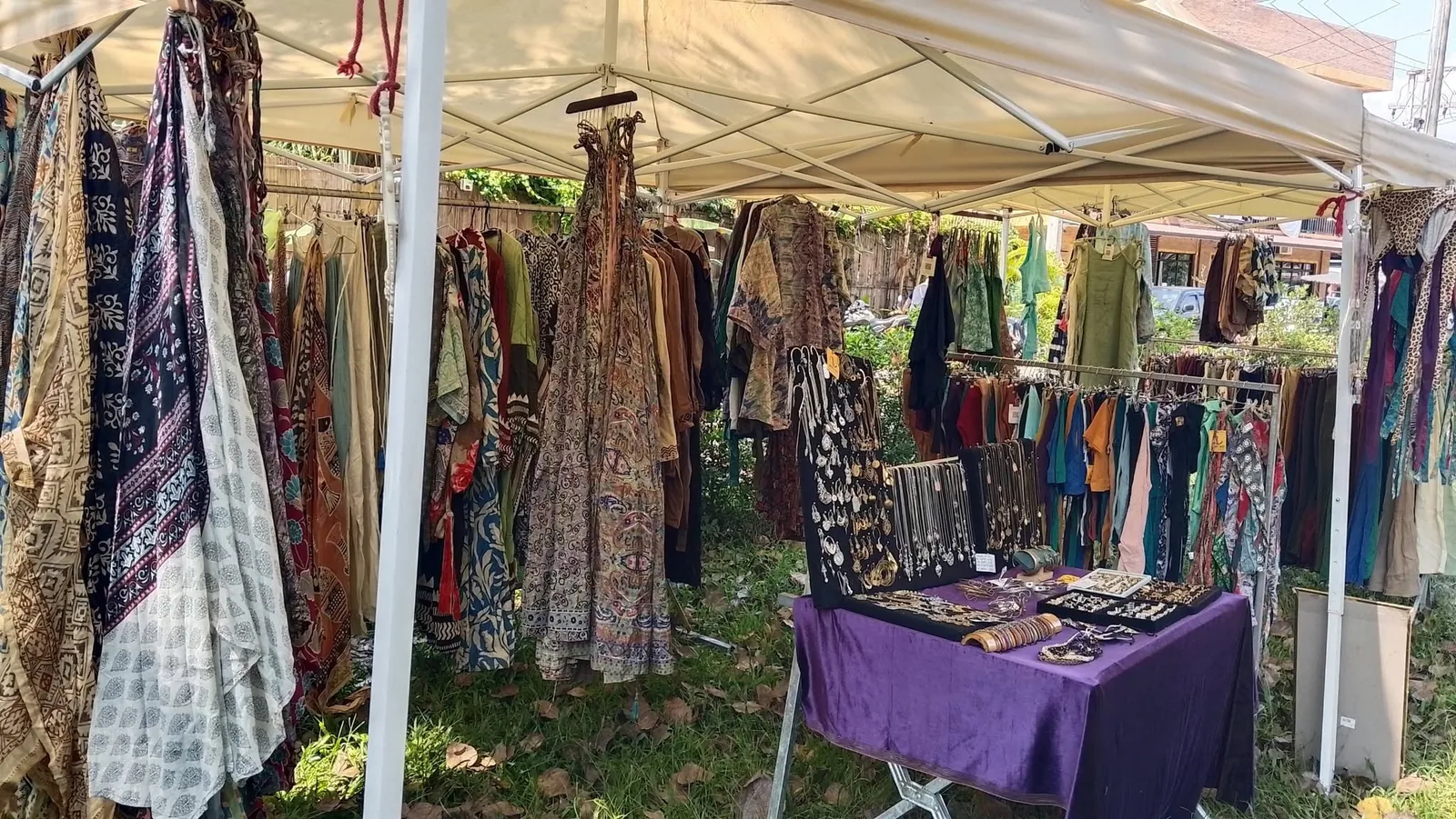 A market stall of patterned dresses, wraps and trousers hanging under a white tent