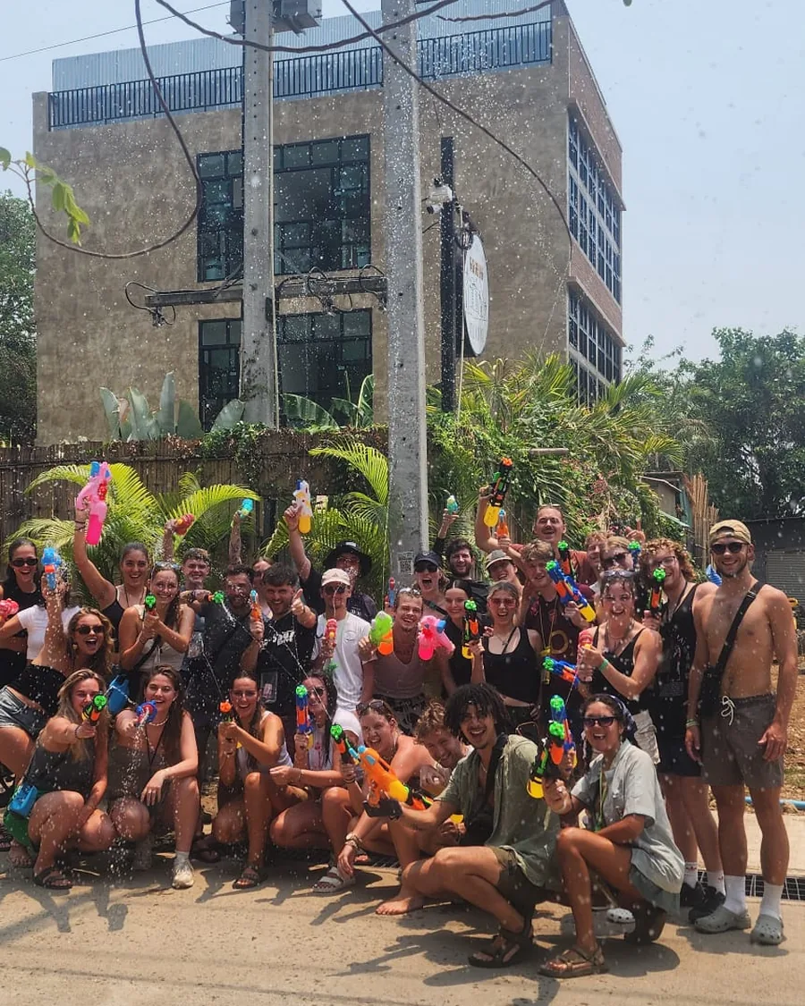 A big Nolo Hub group crouching and standing in the street, soaked and laughing, firing water guns at the camera