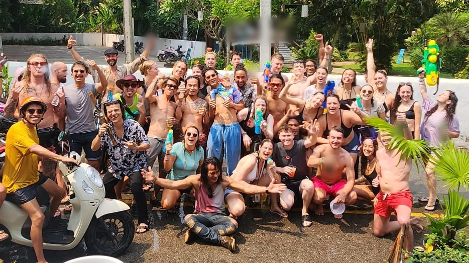 A big Nolo Hub group soaked in the street at Songkran, cheering, with water guns and a scooter at the front