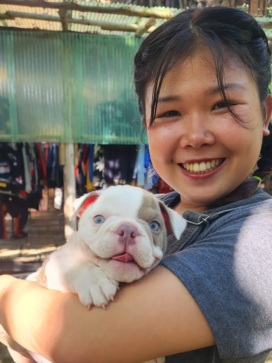 Zeen smiling and holding a white and lilac bulldog puppy