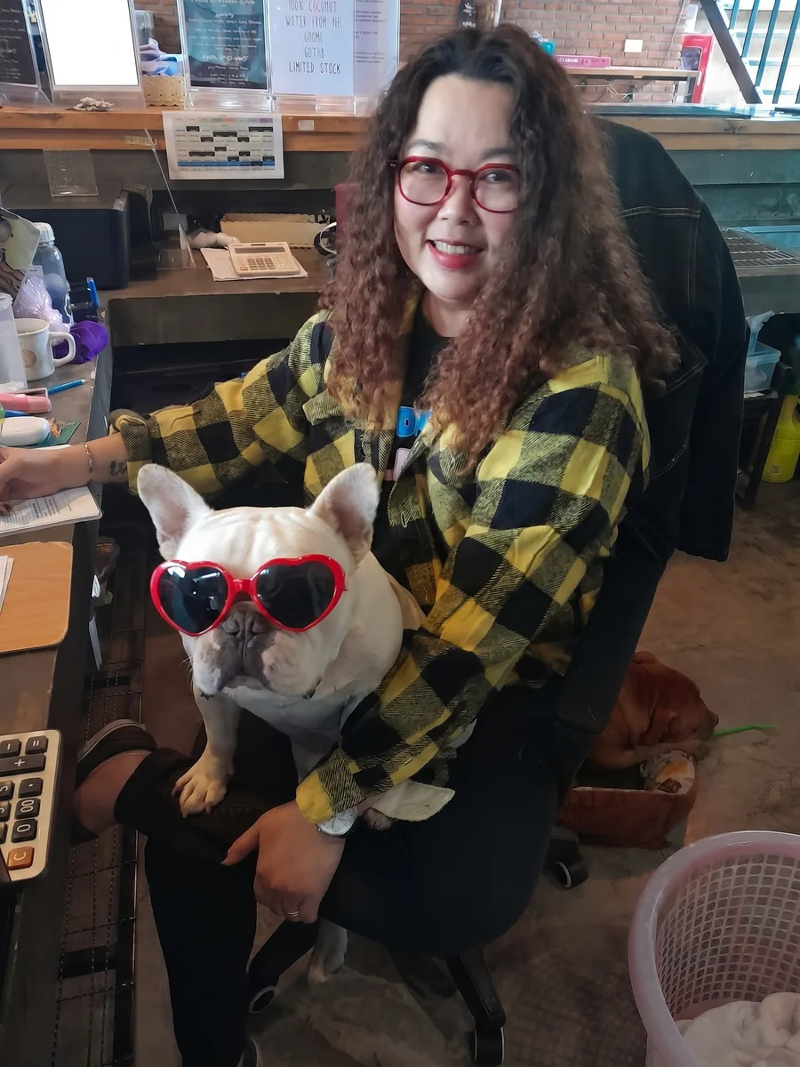 Jeen at the reception desk with a white French bulldog in heart-shaped sunglasses on her lap