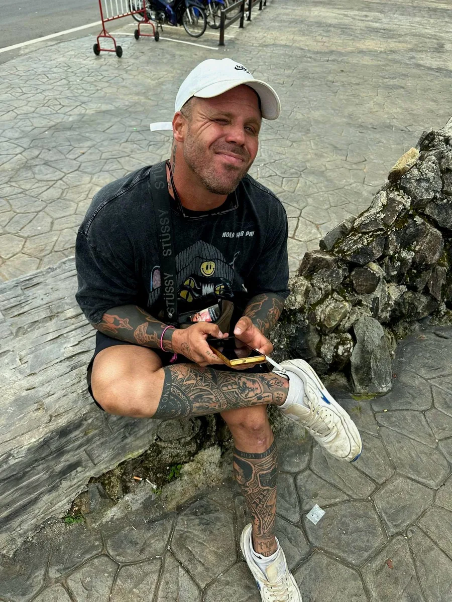 Jordin in a white cap, sitting on a rock by the road with a phone