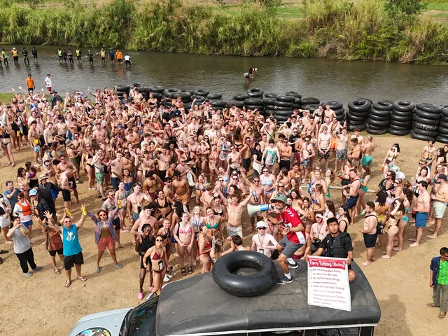 The Tipsy Tubing crowd waving at the drone on the riverbank, tubes stacked by the Pai River