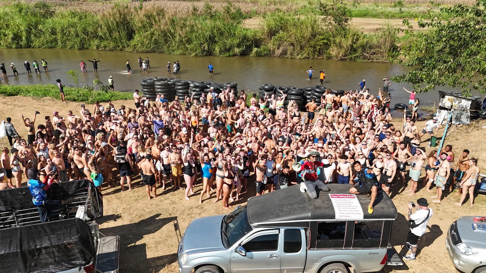 The tubing crowd on the riverbank before the float, the pickup trucks in front and the river behind