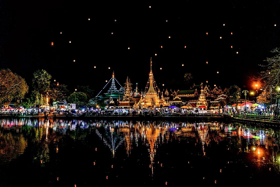 Sky lanterns over Chong Kham Lake at night, the temples lit and reflected in the water